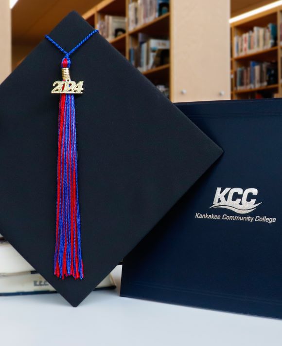 A graduation cap with a "2024" tassel next to a KCC diploma holder