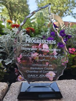 KCC Progress Award - Innovation in Agriculture 2026 Award in front of flowers. Award says Daily Journal Progress2026 Innovation in Agriculture Kankakee Community College Sponsored by Kankakee County Chamber of Commerce Daily Journalge